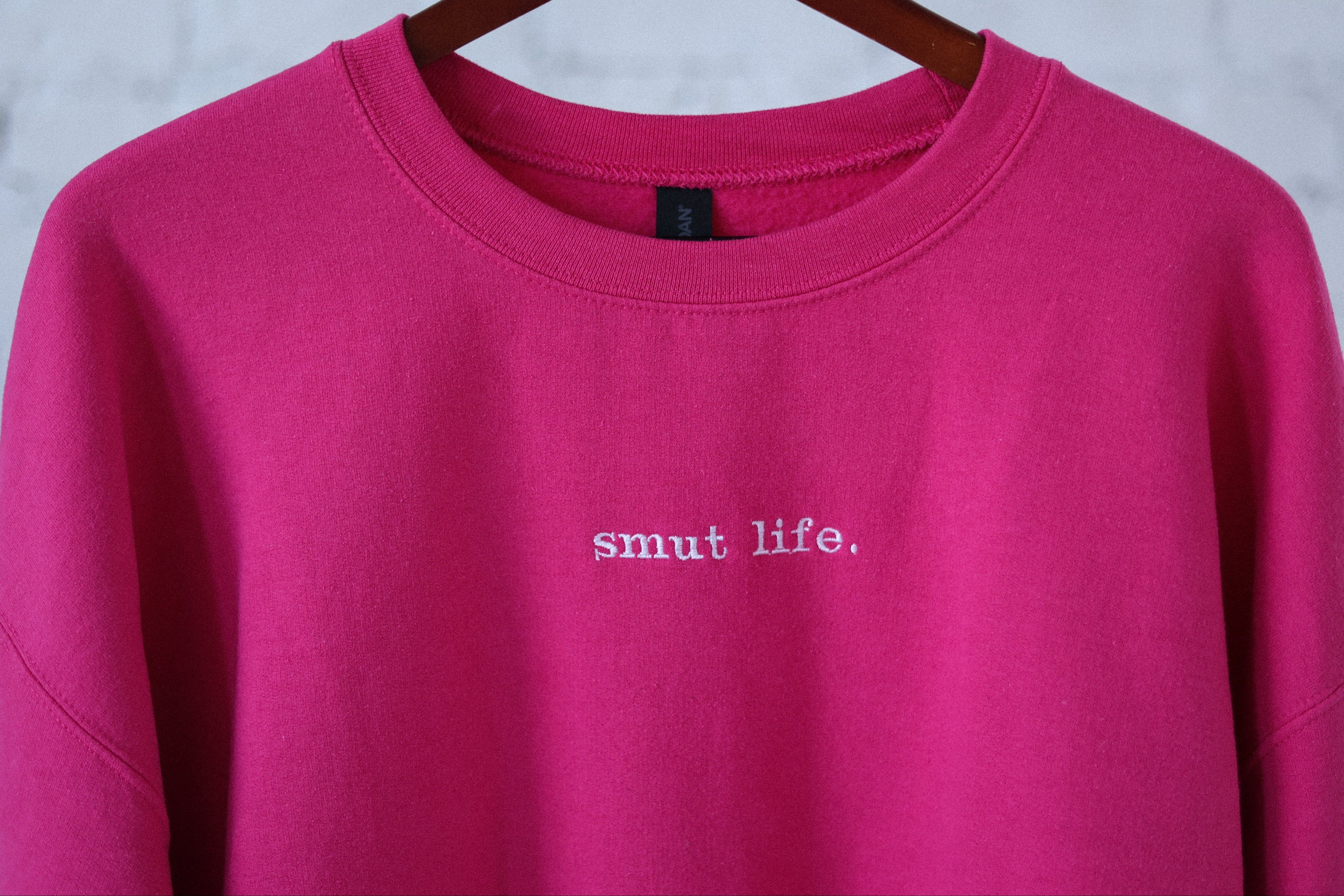 smut life. oversized crewneck in main character (hot pink) on a hanger against a white wall.