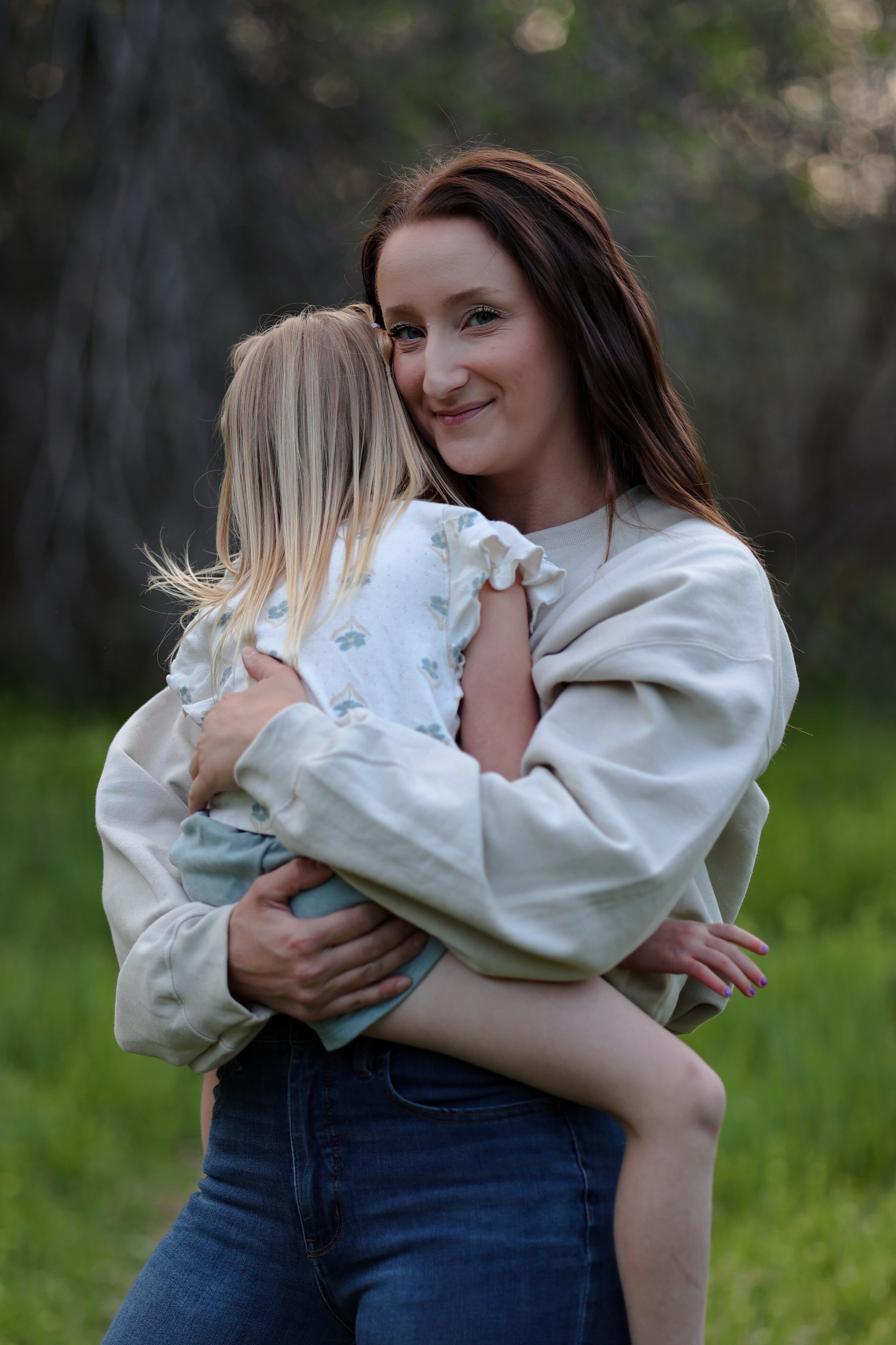Woman holding a child in a grassy outdoor setting in rooted (sand)