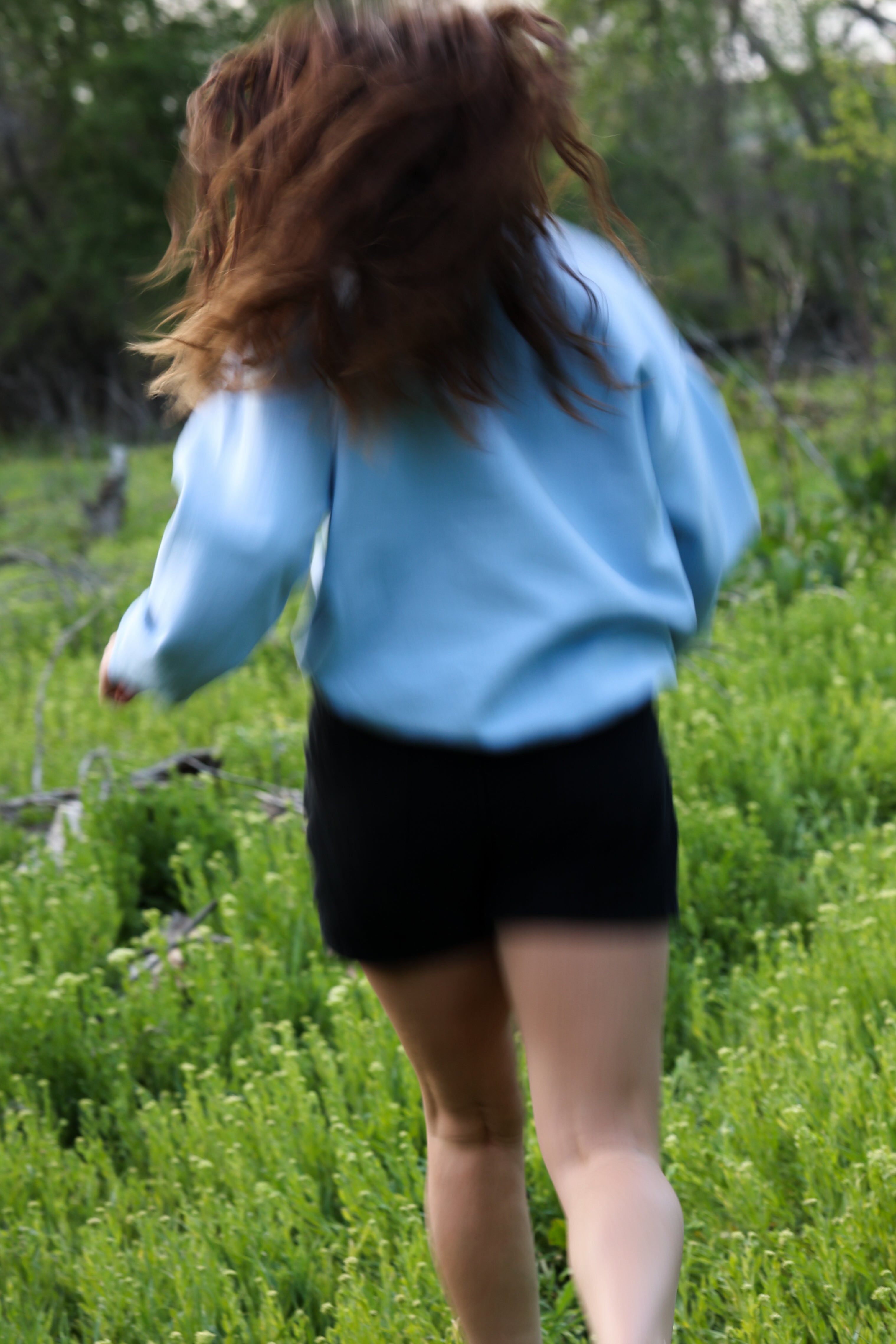 Person in a blue sweater and black shorts running through a grassy field. in steady (light blue)