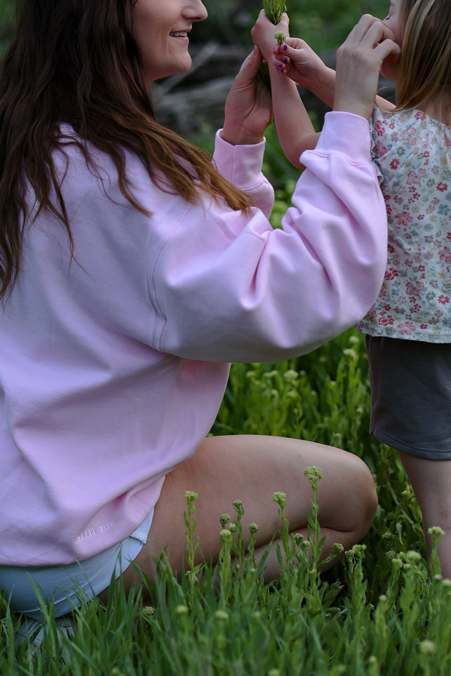 Two people in a grassy area, one wearing a pink sweatshirt. in tender (light pink)